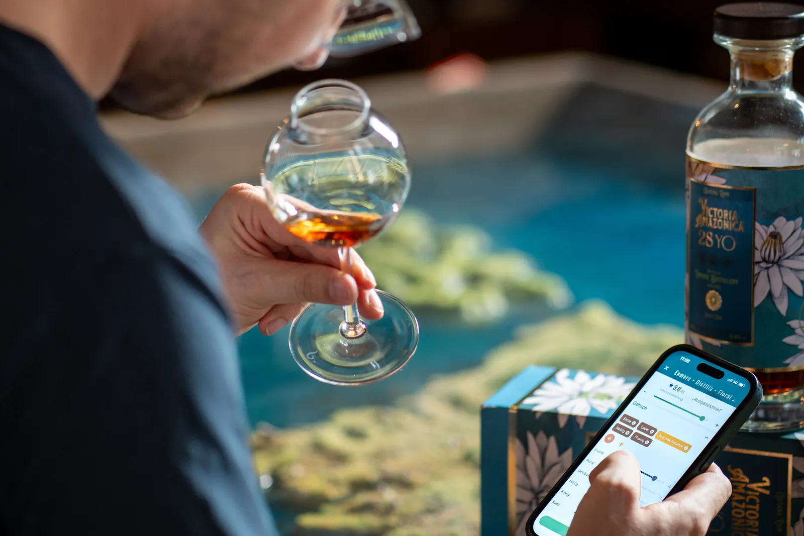 Un utilisateur de RumX hume un rhum ambré dans un verre de dégustation tout en l'enregistrant dans l'app RumX, une bouteille de rhum de 28 ans à côté de lui