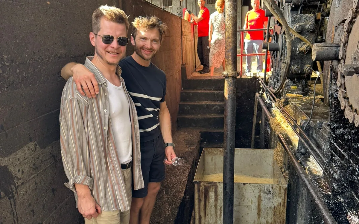 Deux hommes avec un verre de dégustation à côté du moulin à cannes dans une distillerie en activité.