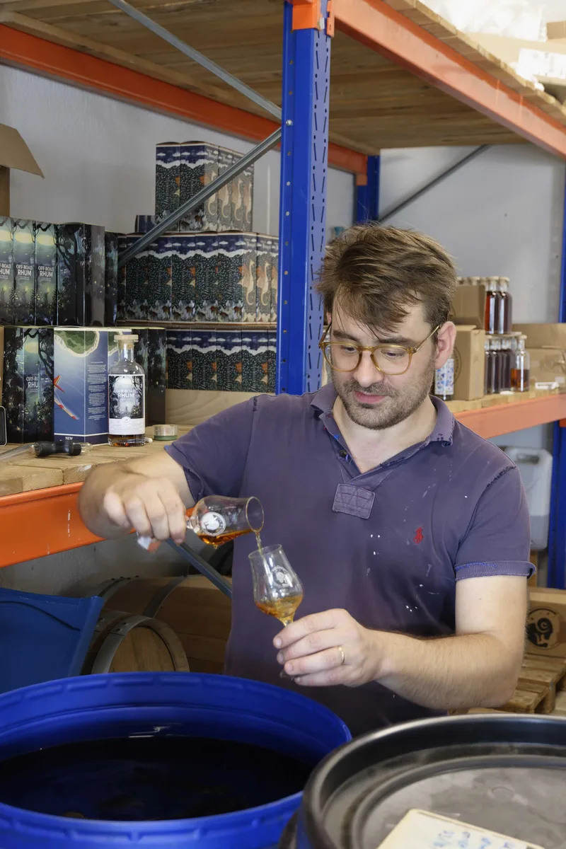 Nicolas Petit gießt eine Fassprobe in ein Nosingglas, dahinter stapeln sich Kartons der Off-Road Rhum Serie.