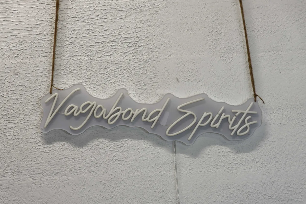Beleuchtetes Vagabond Spirits Schild in weißer Schreibschrift, an einer Schnur an der Kellerwand.