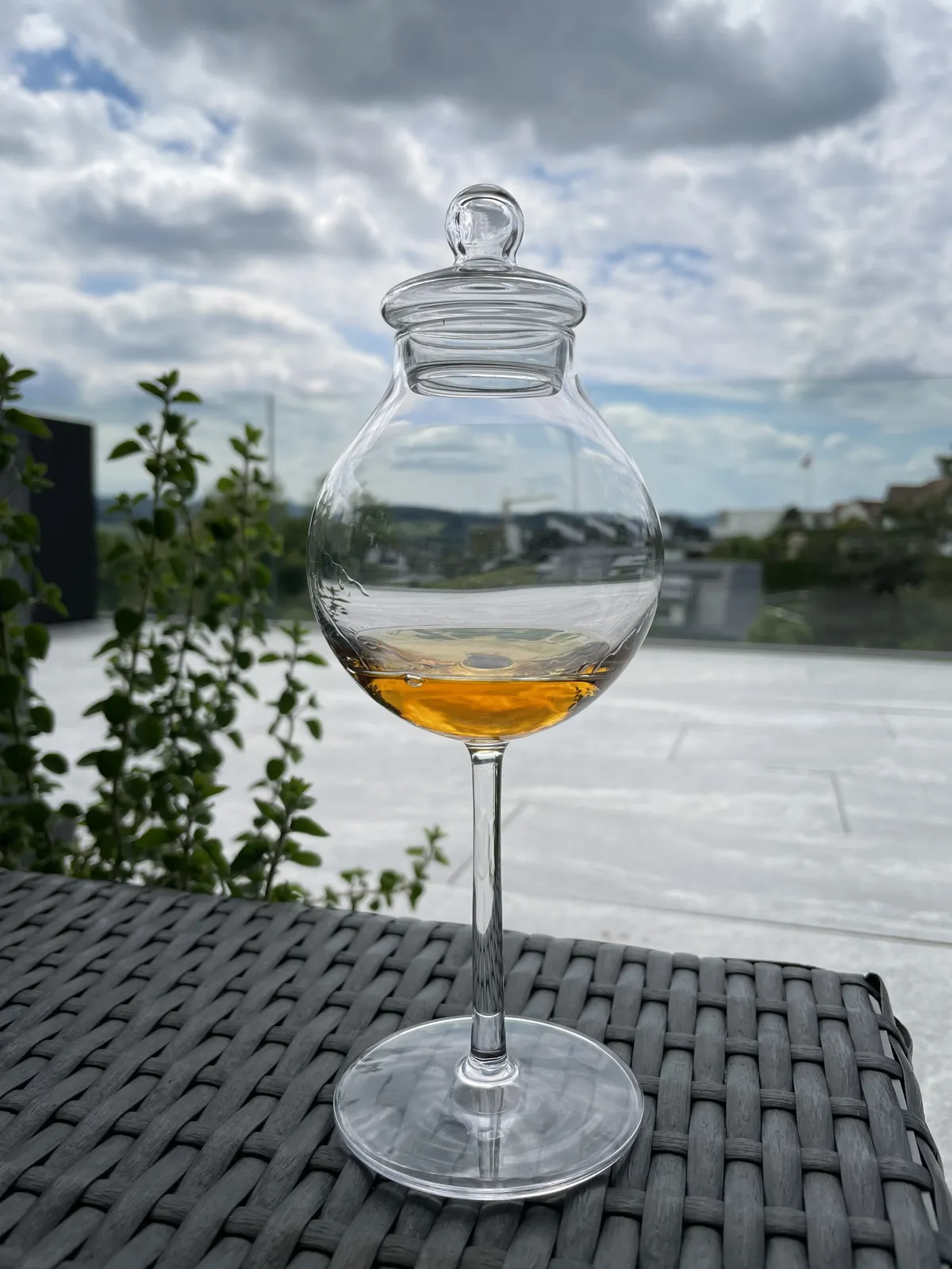 Tulpenförmiges Verkostungsglas mit Knopfdeckel und einem Schluck Rum, im Hintergrund eine Terrasse