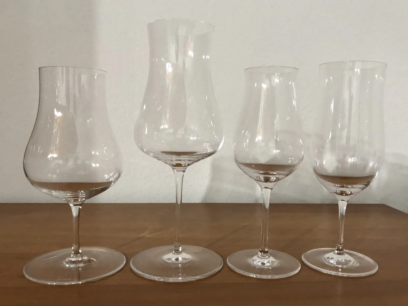 Vier Eisch-Gläser unterschiedlicher Form und Größe nebeneinander auf einem Holztisch