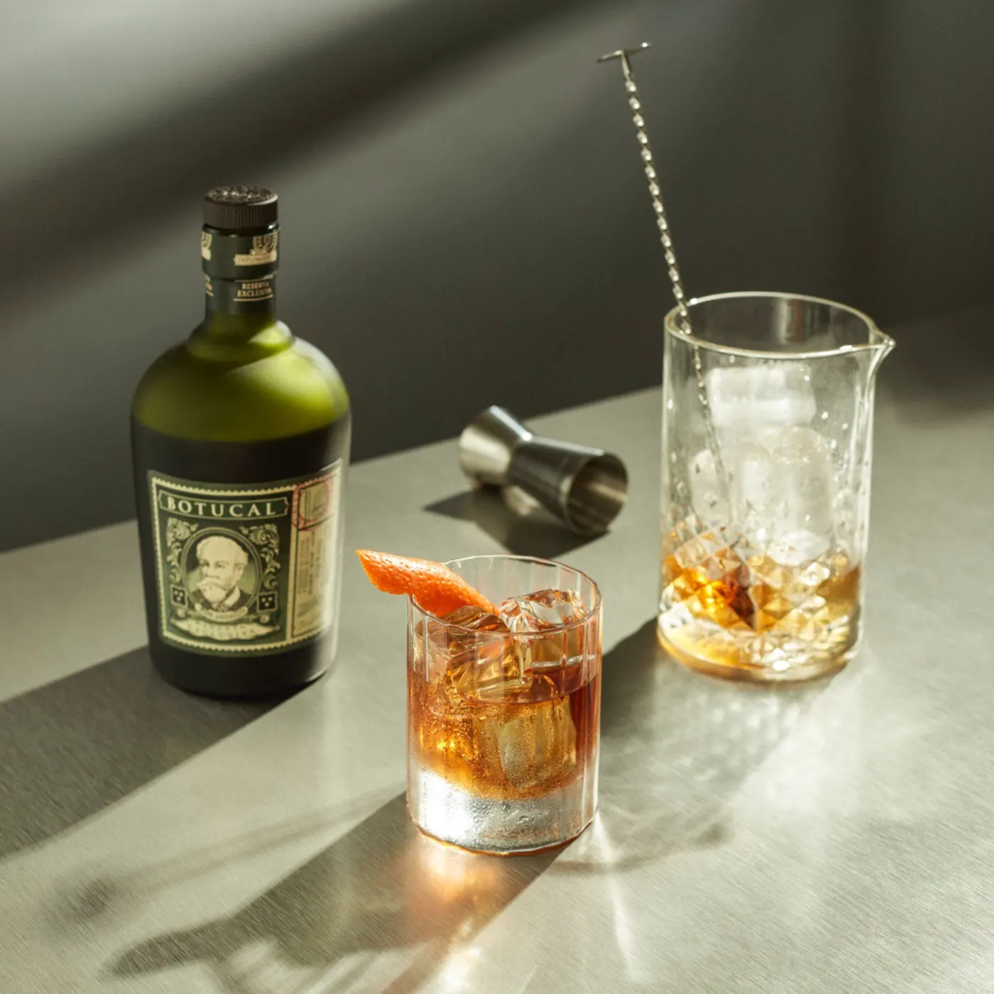 Flasche Diplomático Reserva Exclusiva mit Botucal-Etikett neben einem Old Fashioned mit Orangenzeste und einem Rührglas mit Eis