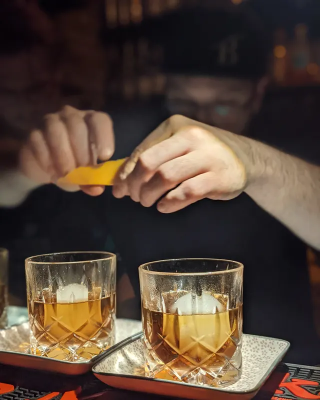 Barkeeper drückt eine Zitruszeste über zwei Old Fashioneds mit großen Eiswürfeln aus