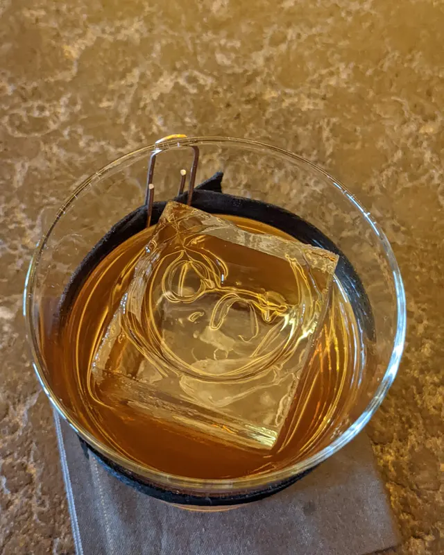 Großer klarer Eiswürfel mit Eiszange im Glas, von oben fotografiert