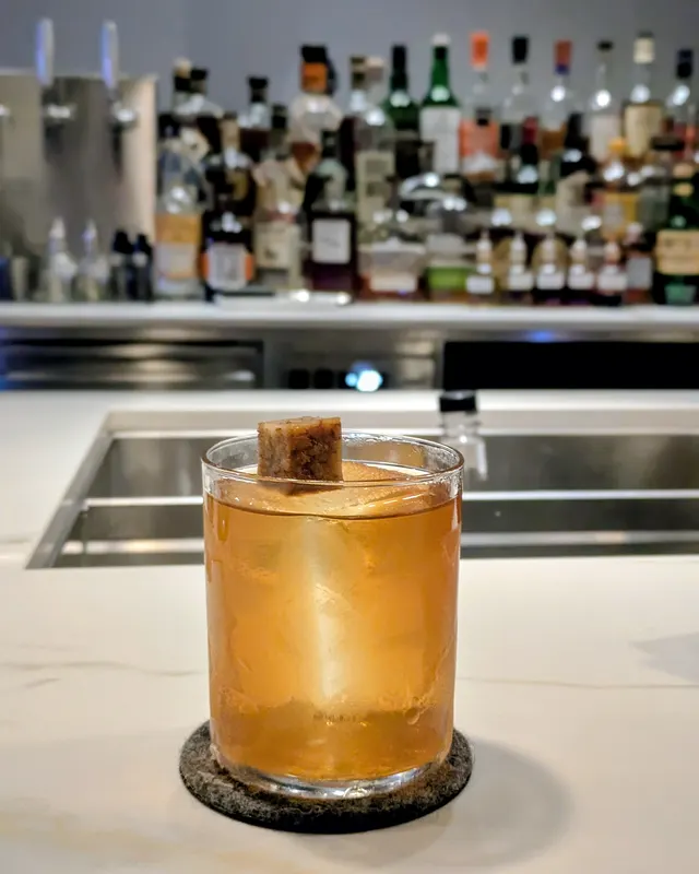 Old Fashioned mit Zimtstange auf heller Marmortheke vor Flaschenregal