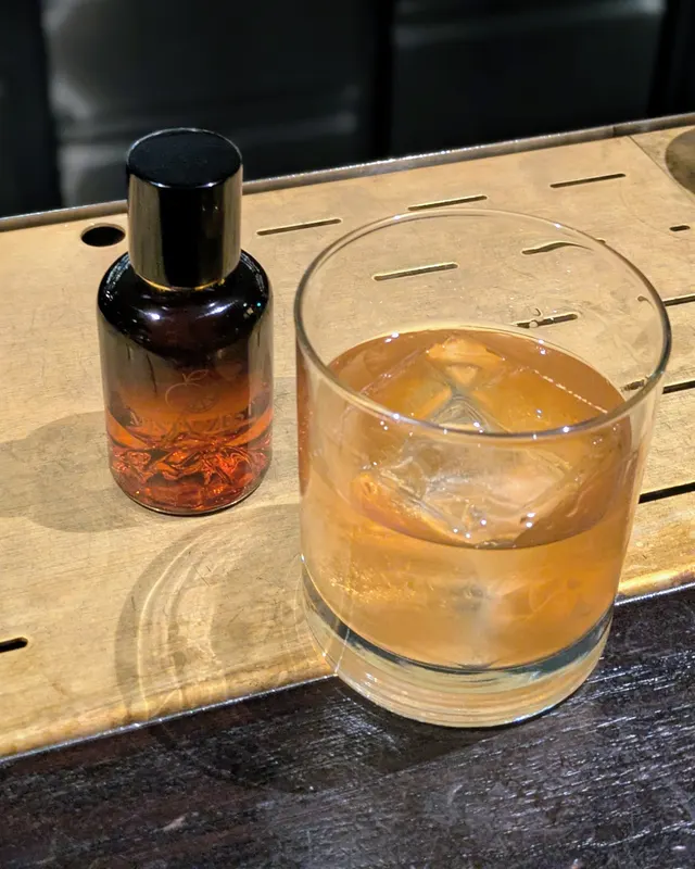 Old Fashioned neben einer kleinen Bitters-Flasche auf einem Holztablett